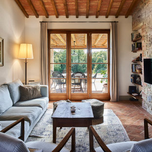 Idee per un soggiorno country di medie dimensioni con pareti beige, pavimento in terracotta, TV a parete, pavimento marrone e pareti in mattoni