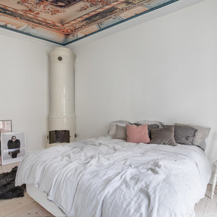 Inredning av ett shabby chic-inspirerat sovrum, med en öppen vedspis, vita väggar, ljust trägolv, en spiselkrans i metall och beiget golv