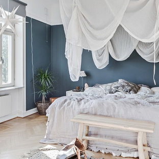 Inredning av ett minimalistiskt sovrum, med blå väggar, ljust trägolv och beiget golv