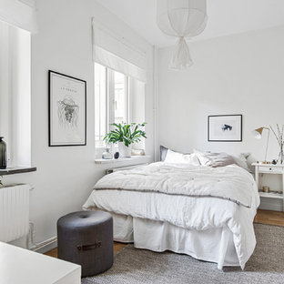 Nordisk inredning av ett sovrum, med vita väggar, mellanmörkt trägolv och brunt golv