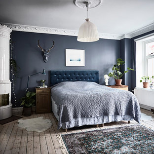 Diseño de dormitorio principal, nórdico, con paredes azules, suelo de madera clara, estufa de leña, marco de chimenea de metal y suelo beige