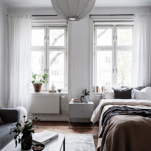 Inredning av ett minimalistiskt sovrum, med vita väggar, mellanmörkt trägolv och brunt golv