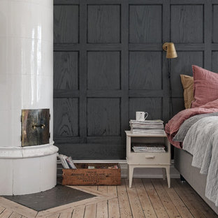 Imagen de dormitorio principal, moderno, de tamaño medio, con chimenea de esquina, paredes negras y suelo de madera clara