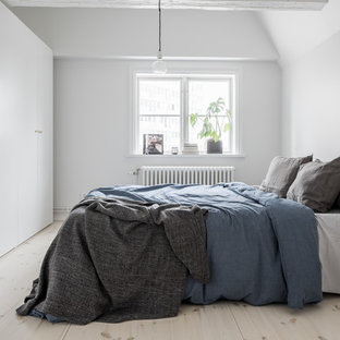 Inredning av ett minimalistiskt mellanstort sovrum, med vita väggar, ljust trägolv och beiget golv