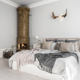 Mittelgroßes Nordisches Hauptschlafzimmer mit gebeiztem Holzboden, weißem Boden, grauer Wandfarbe und Eckkamin in Stockholm