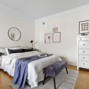 Foto på ett minimalistiskt sovrum, med vita väggar och mellanmörkt trägolv