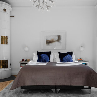 Foto de dormitorio principal, escandinavo, de tamaño medio, con paredes blancas, suelo de madera en tonos medios, estufa de leña, marco de chimenea de baldosas y/o azulejos y suelo beige