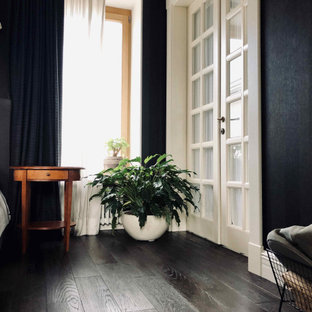 Ejemplo de dormitorio principal, clásico renovado, grande, con paredes negras, suelo de madera oscura, chimenea de esquina, marco de chimenea de metal y suelo negro