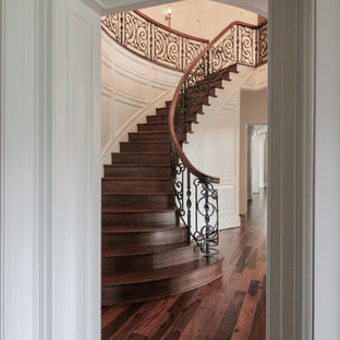 Immagine di una grande scala curva eclettica con pedata in legno, alzata in legno e parapetto in materiali misti