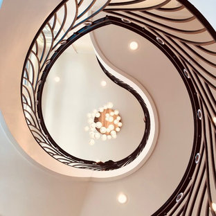 Immagine di una grande scala curva tropicale con pedata in legno, alzata in legno verniciato e parapetto in metallo