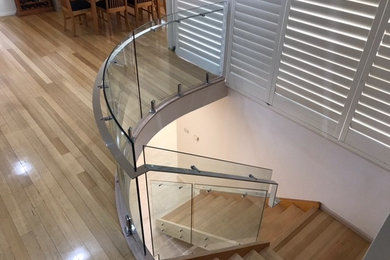 Cette photo montre un grand escalier courbe tendance avec des marches en bois et un garde-corps en métal.
