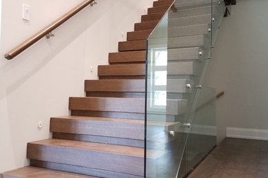 Ejemplo de escalera recta minimalista grande con escalones de madera, contrahuellas de madera y barandilla de vidrio