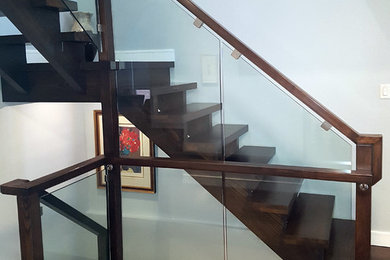 Immagine di una scala a "L" moderna di medie dimensioni con pedata in legno, nessuna alzata e parapetto in vetro