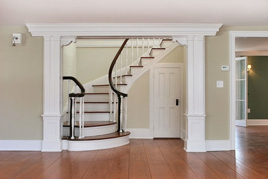 Ejemplo de escalera curva clásica grande con escalones de madera, contrahuellas de madera pintada y barandilla de madera