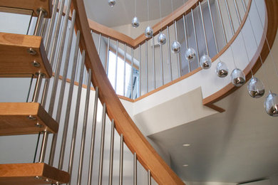 Ejemplo de escalera curva actual de tamaño medio con escalones de madera, contrahuellas de vidrio y barandilla de metal
