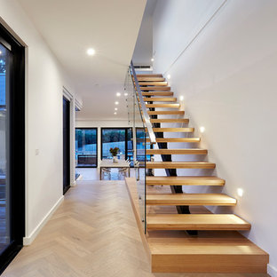 This is an example of a contemporary wood floating staircase in Melbourne with open risers and glass railing.