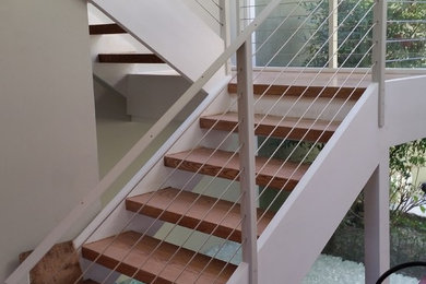 Cette image montre un escalier sans contremarche design en L de taille moyenne avec des marches en bois et un garde-corps en câble.