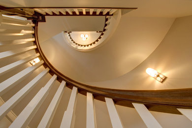Ejemplo de escalera curva de estilo americano grande con escalones de madera, contrahuellas de madera y barandilla de madera