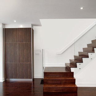 Immagine di una scala minimalista con pedata in legno, alzata in legno e parapetto in vetro