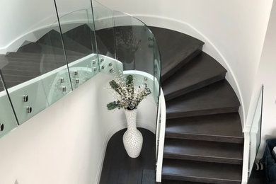 Example of a large minimalist wooden curved glass railing staircase design in Miami with wooden risers