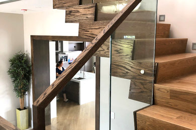 This is an example of a medium sized modern wood u-shaped glass railing staircase in Toronto with wood risers.