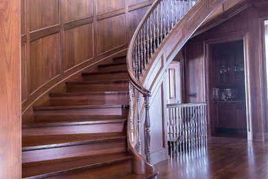 На фото: огромная изогнутая деревянная лестница в классическом стиле с деревянными ступенями