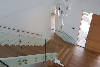 Large minimalist wooden floating open and glass railing staircase photo in Vancouver