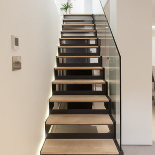 Inspiration for a contemporary wood straight glass railing staircase in London with open risers.