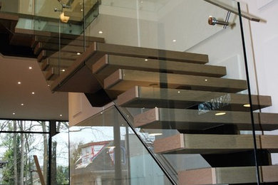 Photo of a large modern metal floating glass railing staircase in Other with metal risers and feature lighting.
