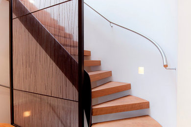Design ideas for a contemporary wood curved staircase in London with open risers and feature lighting.