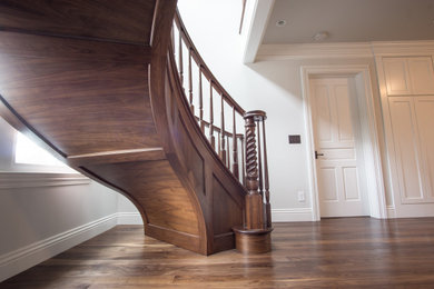 Foto de escalera curva clásica grande con escalones de madera, contrahuellas de madera y barandilla de madera