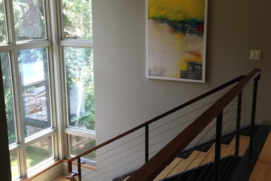 Cette photo montre un grand escalier moderne en L avec des marches en bois, des contremarches en métal et un garde-corps en câble.