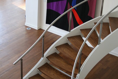 Imagen de escalera curva sin contrahuella con escalones de madera y barandilla de varios materiales