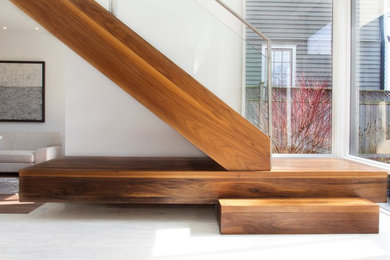 Imagen de escalera en L minimalista sin contrahuella con escalones de madera y barandilla de vidrio