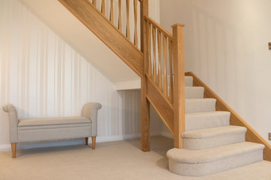 Diseño de escalera en L contemporánea con escalones enmoquetados, contrahuellas enmoquetadas y barandilla de madera