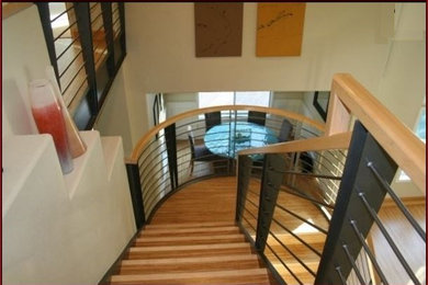 Ejemplo de escalera curva contemporánea grande con escalones de madera, contrahuellas de madera y barandilla de metal