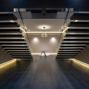 Immagine di una grande scala sospesa minimalista con pedata in legno, nessuna alzata e parapetto in vetro