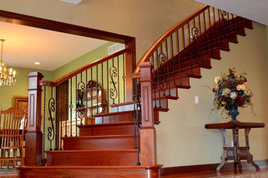 Imagen de escalera curva clásica grande con escalones de madera, contrahuellas de madera y barandilla de varios materiales