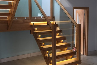 Medium sized contemporary wood u-shaped glass railing staircase in Other with feature lighting.