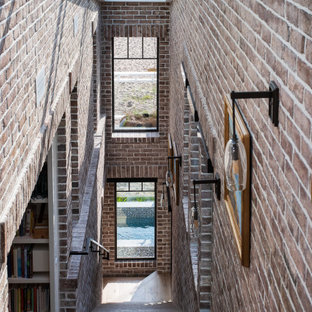 Idee per una grande scala a rampa dritta costiera con pedata in legno, alzata in legno, parapetto in metallo e pareti in mattoni