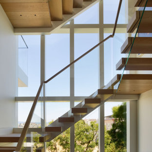 Immagine di una grande scala a "U" minimal con pedata in legno, nessuna alzata e parapetto in vetro