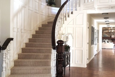 Стильный дизайн: большая изогнутая лестница в стиле кантри с ступенями с ковровым покрытием, ковровыми подступенками и деревянными перилами - последний тренд