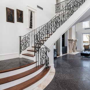 Diseño de escalera curva, mediterránea, grande, con escalones de madera, barandilla de metal y contrahuellas de travertino