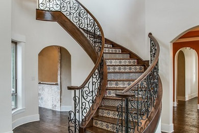 Aménagement d'un escalier courbe méditerranéen avec des marches en bois, des contremarches carrelées et un garde-corps en métal.