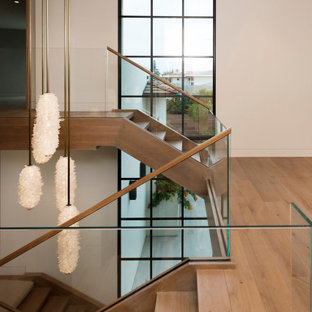 Foto di una grande scala a "U" minimalista con pedata in legno, nessuna alzata e parapetto in vetro