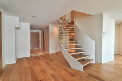 Staircase - large modern wooden curved open and glass railing staircase idea in Montreal
