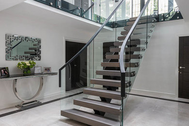 Large contemporary wood curved glass railing staircase in West Midlands with open risers.