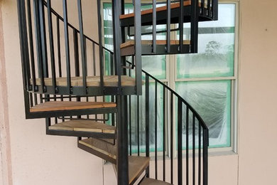 Medium sized traditional wood spiral metal railing staircase in Charleston with open risers.
