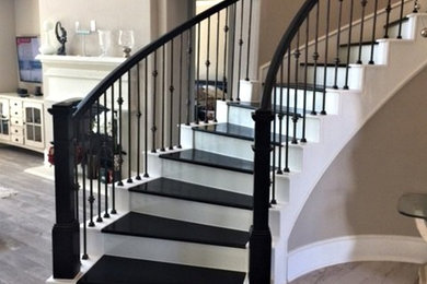 Photo of a large modern wood curved metal railing staircase with painted wood risers.