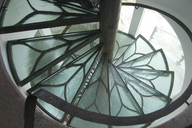 Cette image montre un escalier courbe design de taille moyenne avec des marches en verre, des contremarches en verre et un garde-corps en métal.